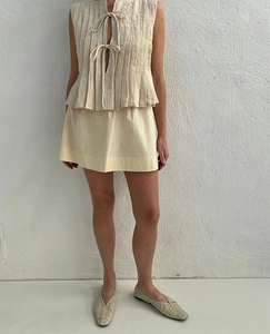 Detail of beige pleated tie-front vest and yellow skirt in natural linen fabric