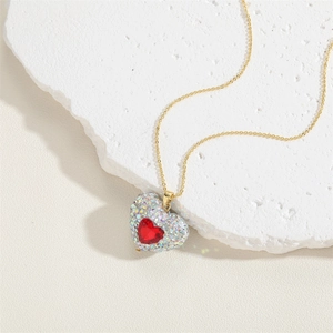 Detailed view of a gold heart pendant with a red gemstone and pavé stones on a marble surface