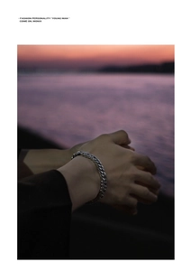 Close-up of silver Cuban link bracelet on wrist with sunset water background