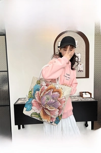 Detailed macro view of the colorful peony embroidery and braided rope handle on the canvas tote bag