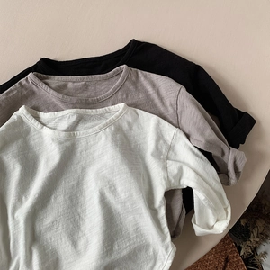Close-up of stacked long-sleeve cotton tees in white, grey, and black with slub texture
