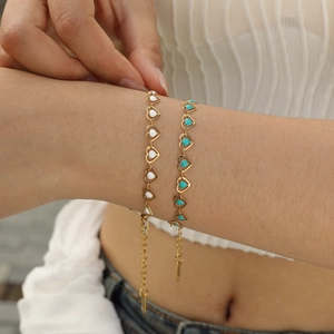 Gold heart link bracelet with white and turquoise enamel details on female wrist