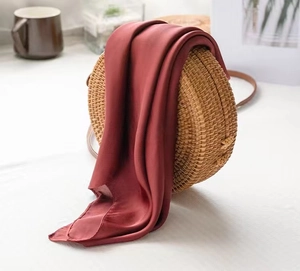 Macro detail of a dark red silk square scarf draped on a woven rattan handbag