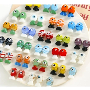 Macro shot of colorful glass fish charms for DIY jewelry making on white textured tray