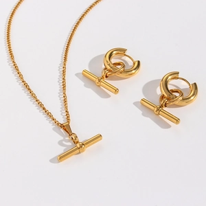 Detail of gold T-bar pendant necklace and matching earrings set on neutral background