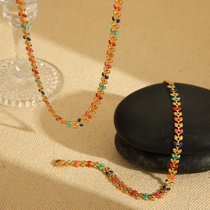 Detail of gold necklace featuring colorful enamel leaf charms on textured beige fabric
