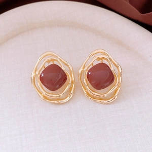 Macro detail of irregular golden earring with brownish resin inlay on a beige tray