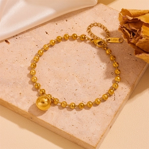 Detail of gold bead chain bracelet with spherical pendant on silk background
