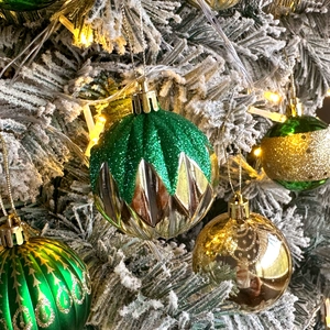 Macro detail of textured green and gold Christmas balls with glitter on snowy tree branches