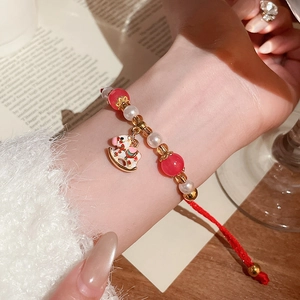 Gros plan du bracelet tressé rouge avec perles et pendentif en forme de cheval à bascule