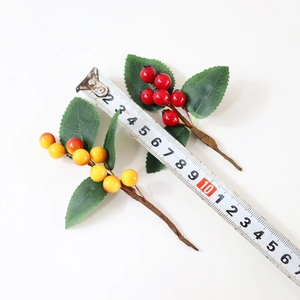 Detail view of artificial berry stems in red and orange with a ruler for size measurement