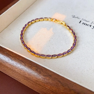 Macro detail of elegant gold-plated bracelet featuring oval purple gemstones on tray