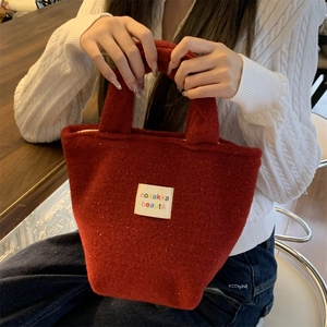 Detail of red plush felt tote bag with white fabric logo patch being held by a model