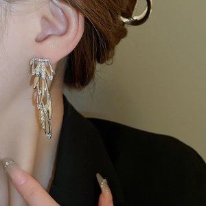 Close-up of sparkling silver tassel earrings with zircon leaf wing design on model