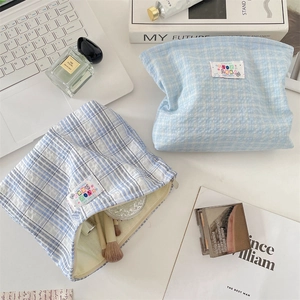 Flat lay of light blue plaid cosmetic bag with laptop and perfume on desk