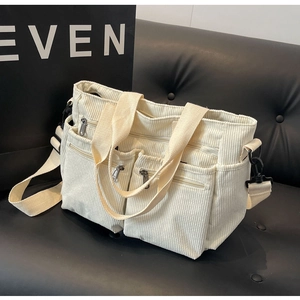 Detail view of cream corduroy crossbody bag with multiple pockets on black leather background