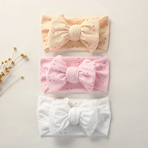 Three soft nylon baby headbands in peach, pink and white with hollow bow detail