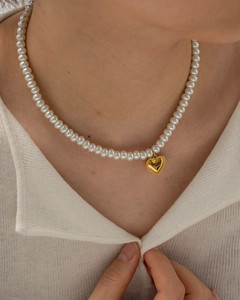 Elegant white pearl necklace with a golden heart pendant worn on the collarbone