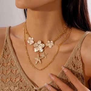 Detail of layered gold necklaces with metallic flowers and starfish on a model