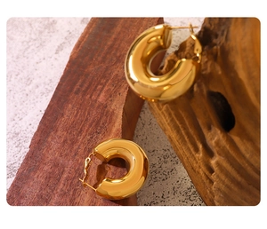 Close-up of gold-plated thick C-shaped hoop earrings on dark wood and stone background