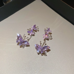 Close-up of purple zircon butterfly ear cuffs on a beige textured jewelry tray