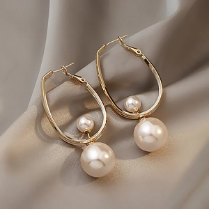 Close-up of gold U-shaped earrings with two white pearls on grey silk fabric background