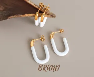Detailansicht der U-förmigen Gold-Weiß-Emaille-Ohrringe auf beige Travertin-Stein