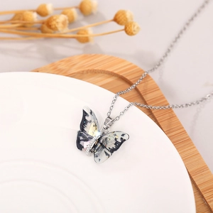 Detail of butterfly necklace with artistic ink texture pendant on a white ceramic plate
