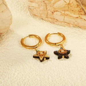 Golden star-shaped earrings with shell texture and eye pattern on sand and stone