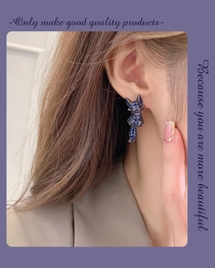 Close-up of a fox-shaped earring with blue crystals on a model’s ear for scale