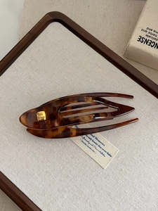 Detail view of large tortoiseshell hair clip with fashion logo on wood linen tray