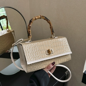 Detail of beige crocodile pattern handbag with bamboo handle and gold twist lock