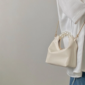 Close-up of cream pillow bag featuring a pearl top handle and golden chain shoulder strap