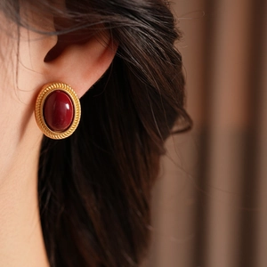 Close-up of vintage oval earring with red gemstone and gold textured border on model
