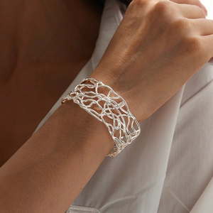 Detail of silver woven hollow mesh cuff bracelet worn on wrist over white clothing