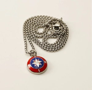 Detailed close-up of a nautical compass pendant with red and blue enamel and silver star