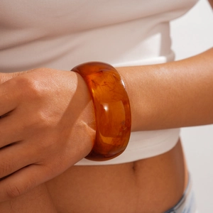 Macro shot of wide amber resin bangle with marbled textures and high-polish finish