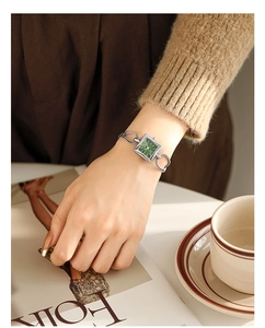 Elegant emerald green square dial watch with gold chain bracelet on woman's wrist