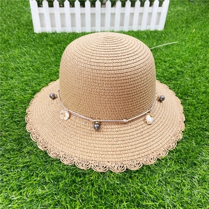 Détail d'un chapeau de paille à larges bords avec perles grises et breloques en coquillage