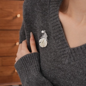 Macro shot of feather brooch with zircons and mother-of-pearl on a grey knit sweater