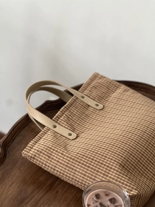 Close-up of vintage gingham canvas tote with leather handles and metal rivets on wood