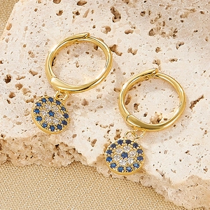 Detail of gold evil eye hoop earrings with blue and white zircons on a textured stone base