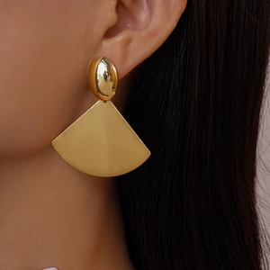 Macro shot of large golden geometric fan earrings featuring brushed metal texture and studs