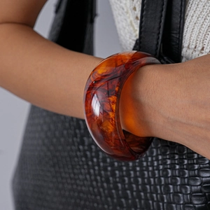 Close-up of a chunky amber resin bangle with marbled texture worn by a model