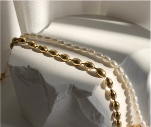Detail of layered pearl necklace and 18K gold plated metal bead choker on stone