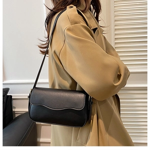 Detail of black crossbody bag with wavy edge and gold hardware on khaki trench coat