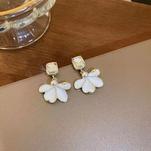 Close-up of elegant flower earrings with white petals, pearls, and crystals on gold base
