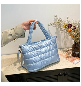 Detailed view of light blue quilted puffer tote with glossy finish on marble surface
