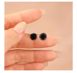 Close-up of minimalist black onyx round stud earrings held by hand for size reference
