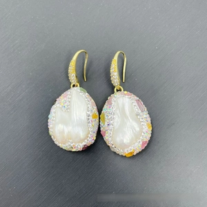 Macro detail of baroque pearl earrings with rainbow crystal borders and gold hooks